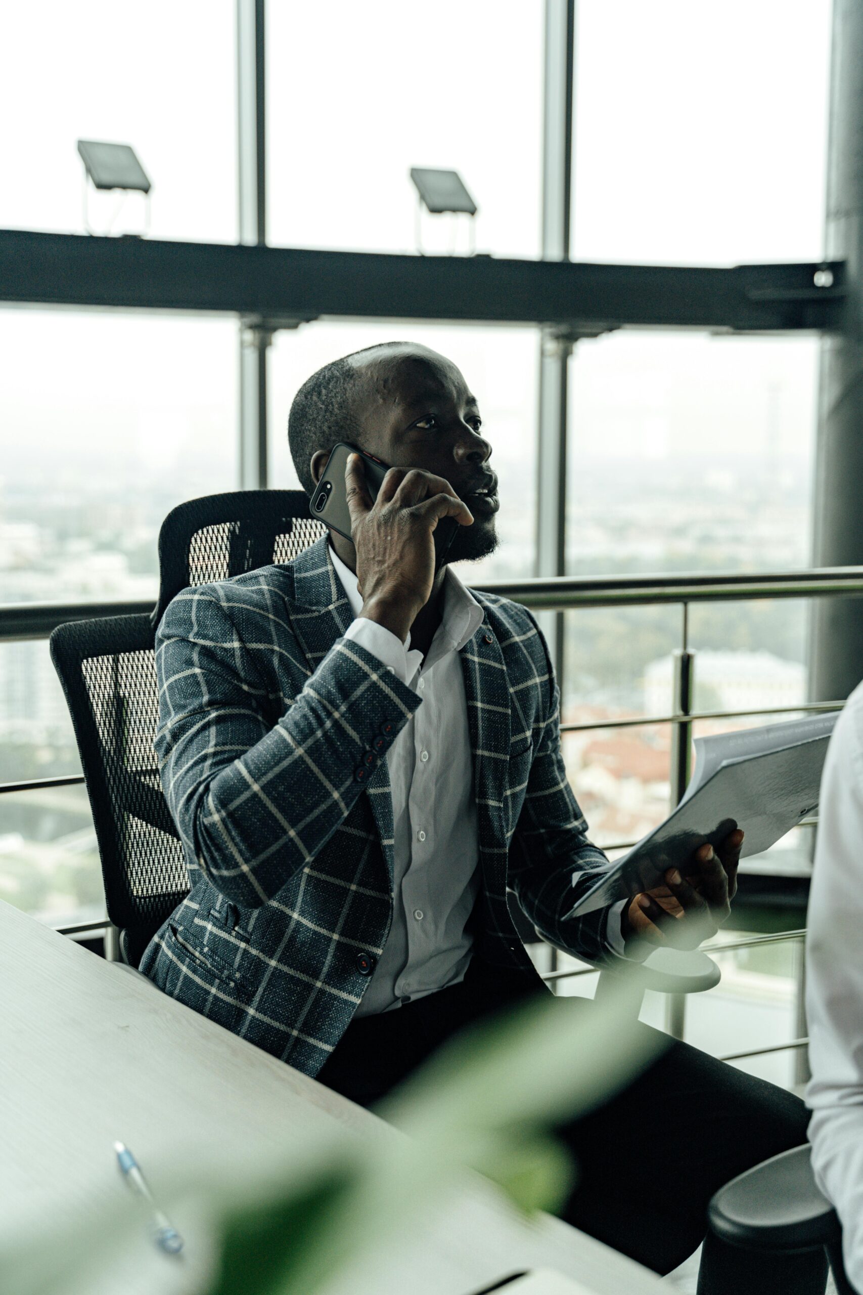 pexels-photo-5583960-5583960 Focused businessman talking on smartphone while holding a document in a modern office setting.